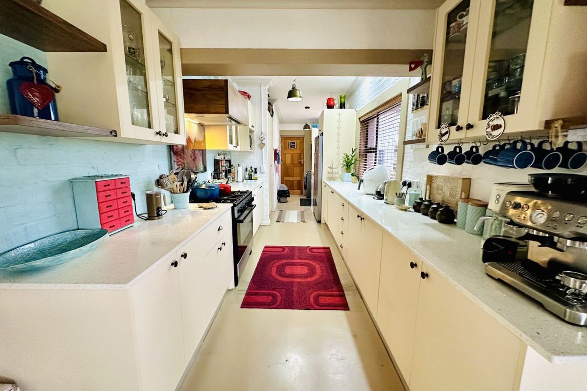 A galley-style kitchen featuring light-toned cabinetry, stone countertops, a built-in oven with extractor fan, and open shelving.