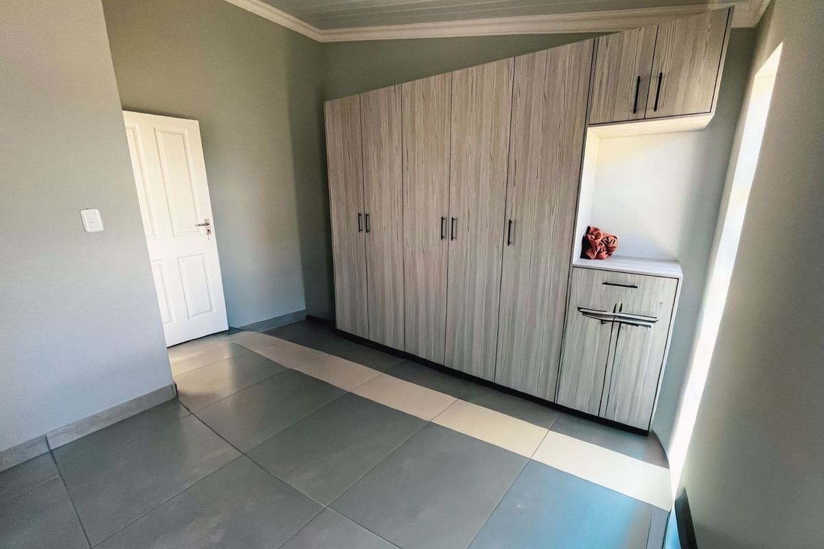 A bedroom featuring built-in cabinetry with a light wood-grain finish, tiled flooring, and a neutral color palette.