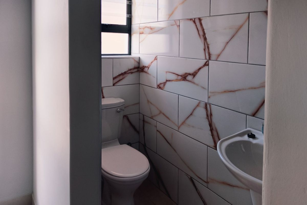 A compact bathroom featuring modern marble-effect wall tiling, a white ceramic toilet, and a pedestal basin with a window for natural light.