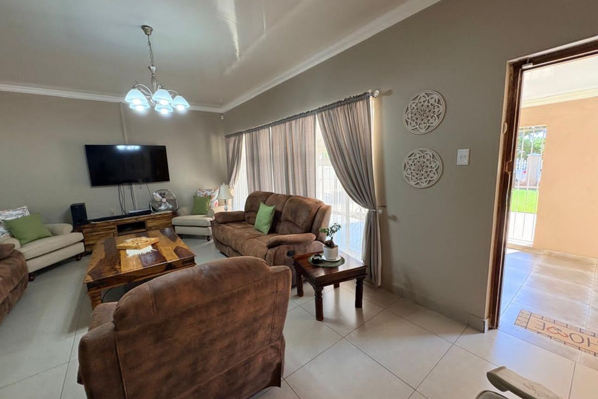 A comfortable living room featuring neutral tiled flooring, large windows with curtains, and a direct entrance to an outdoor patio area.