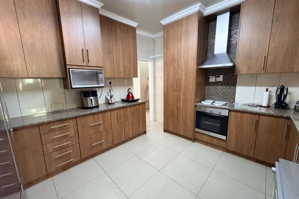 A well-maintained kitchen featuring wood-finish cabinetry, granite countertops, a built-in oven, stainless steel extractor fan, and tiled flooring.