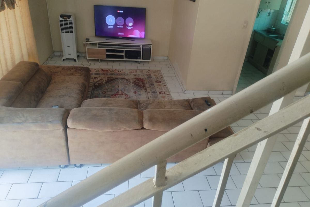 A living room area featuring tiled flooring and a staircase, with an adjacent view into a kitchen space.