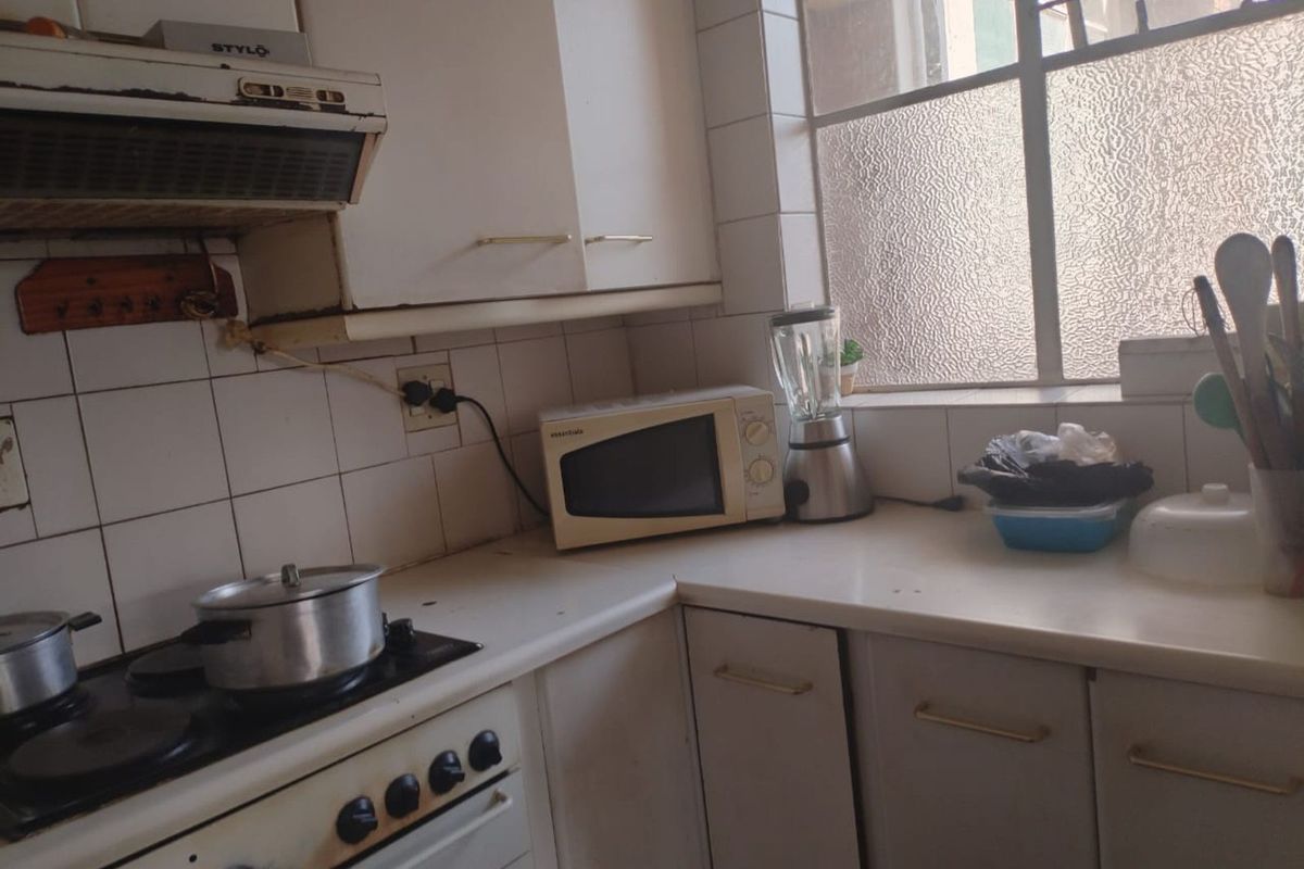 A compact kitchen featuring white cabinetry, tiled splashbacks, a built-in stove with extractor fan, and a window providing natural light.