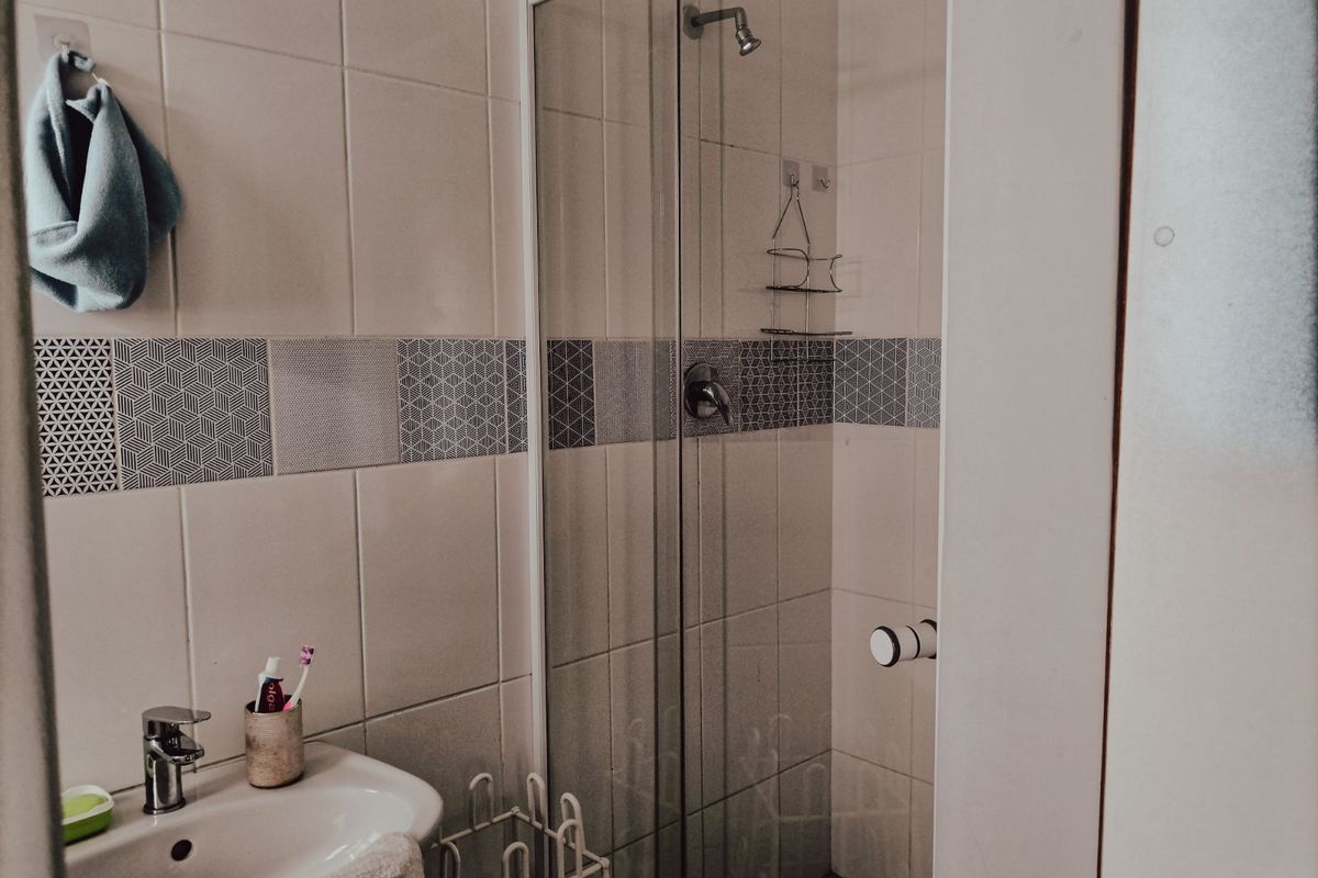 A functional bathroom featuring a glass-enclosed shower, wall-mounted shower head, and a pedestal basin with modern geometric accent tiling.