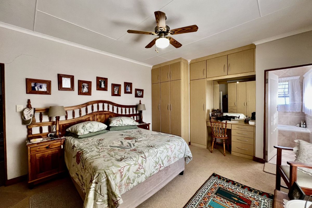 Spacious bedroom featuring built-in wooden cabinetry with integrated vanity, ceiling fan, and direct access to an en-suite bathroom.