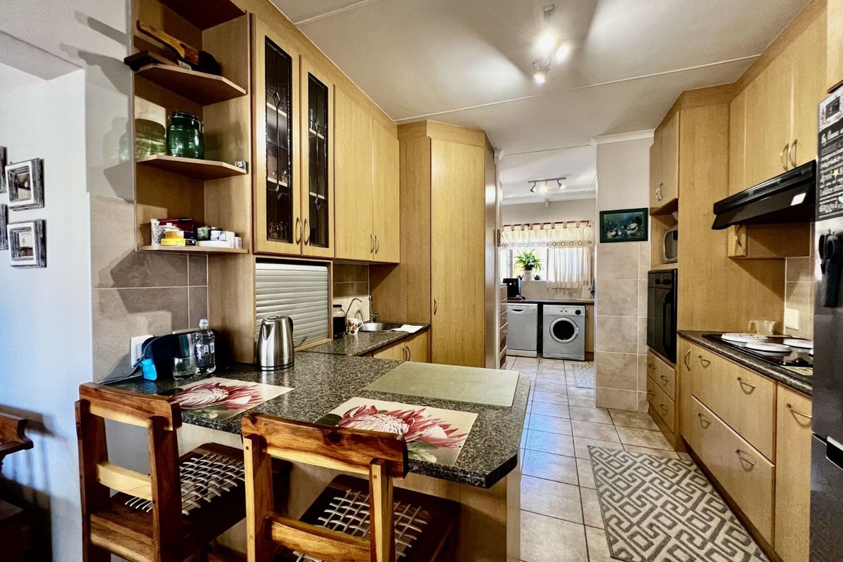 A functional kitchen featuring light wood cabinetry, granite-look countertops, a breakfast bar, and an integrated laundry area with tiled flooring throughout.