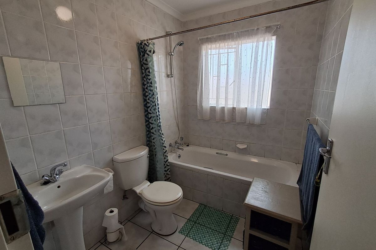 A functional bathroom featuring a pedestal basin, toilet, and a bathtub with an overhead shower attachment, finished with neutral wall and floor tiles.