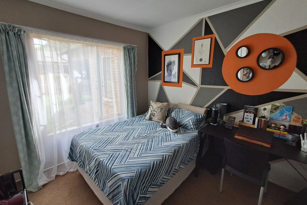 A bedroom featuring a large window with natural light, carpeted flooring, and a decorative geometric accent wall.