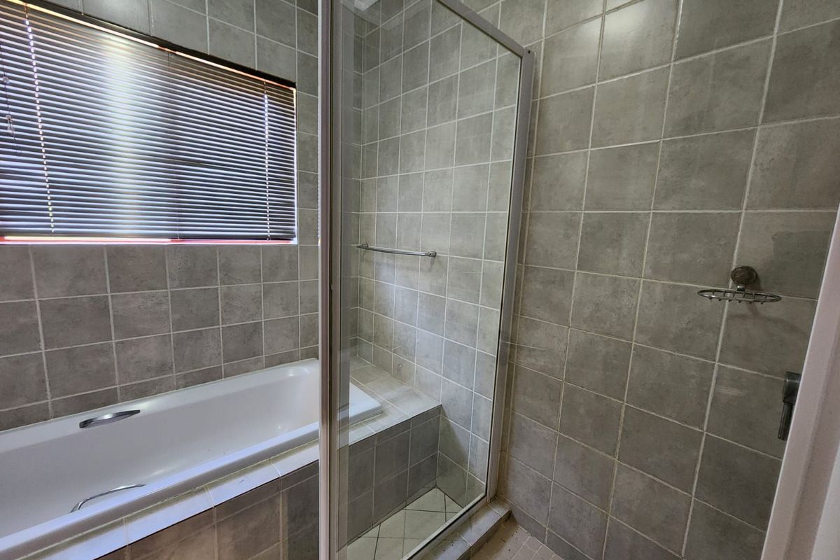 A functional bathroom featuring a built-in bathtub, a separate glass-enclosed shower, and neutral wall tiling.