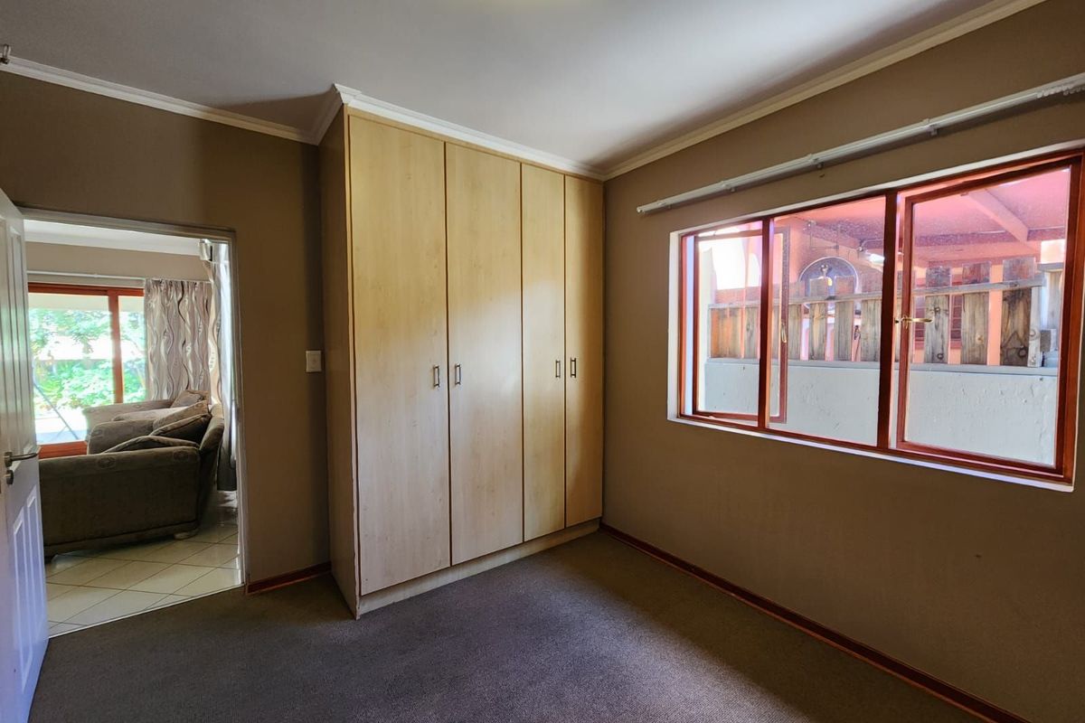 A bedroom featuring built-in wooden cupboards, carpeted flooring, and a window overlooking an outdoor area.