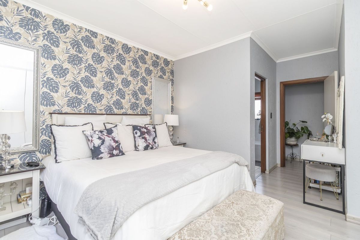 A well-maintained bedroom featuring patterned wallpaper, light-toned laminate flooring, and an adjoining en-suite bathroom.