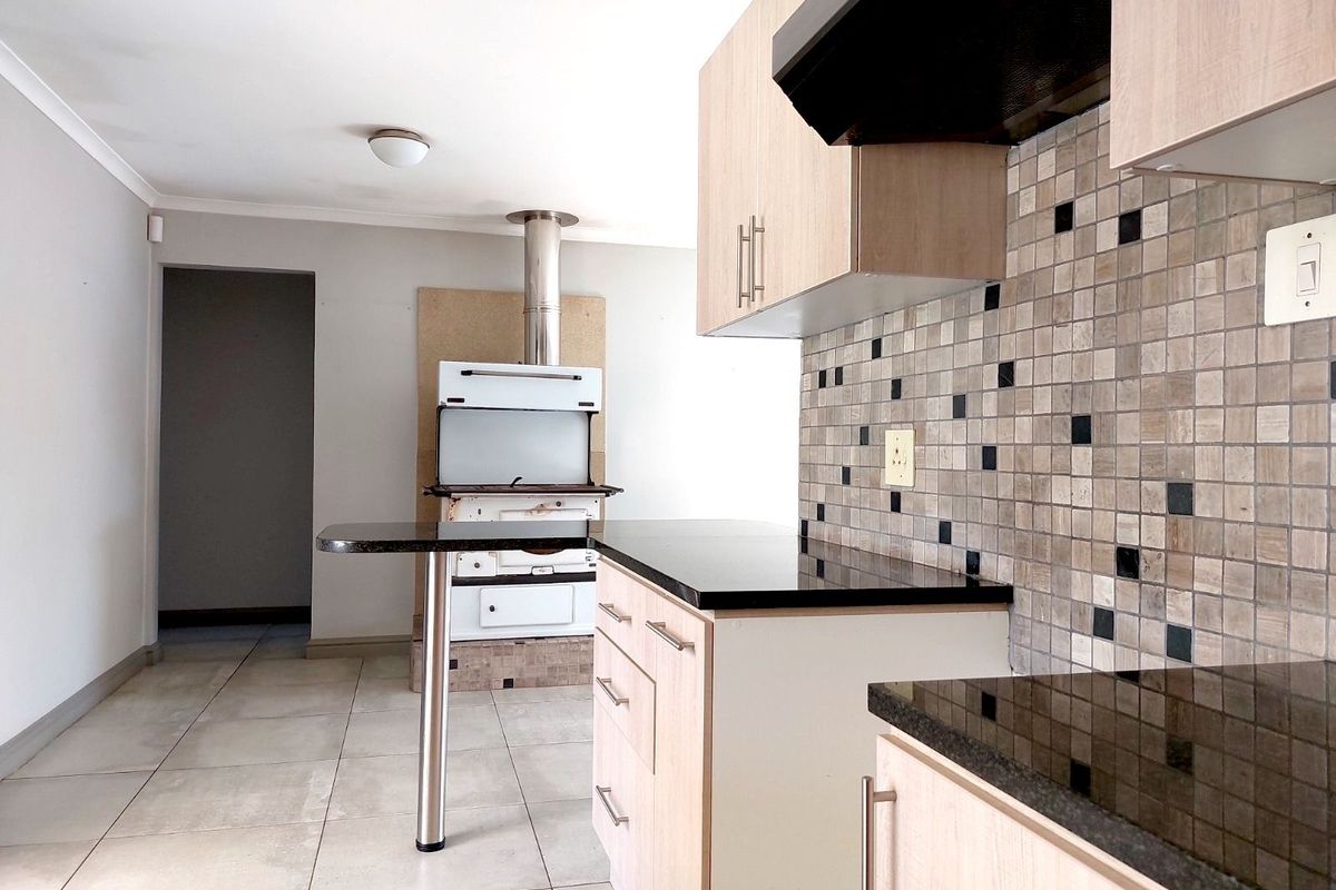 Kitchen featuring light wood-finish cabinetry, black granite countertops, mosaic tile backsplash, and a built-in stove with stainless steel extractor hood.