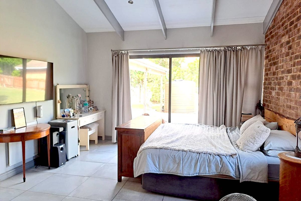 Spacious bedroom featuring exposed brick feature wall, vaulted ceilings with exposed beams, tiled flooring, and sliding glass doors leading to the outdoor area.