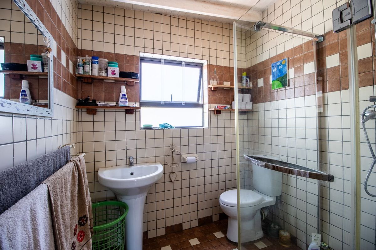 A functional bathroom featuring a pedestal basin, a glass-enclosed shower, and a toilet, finished with classic square wall tiles.