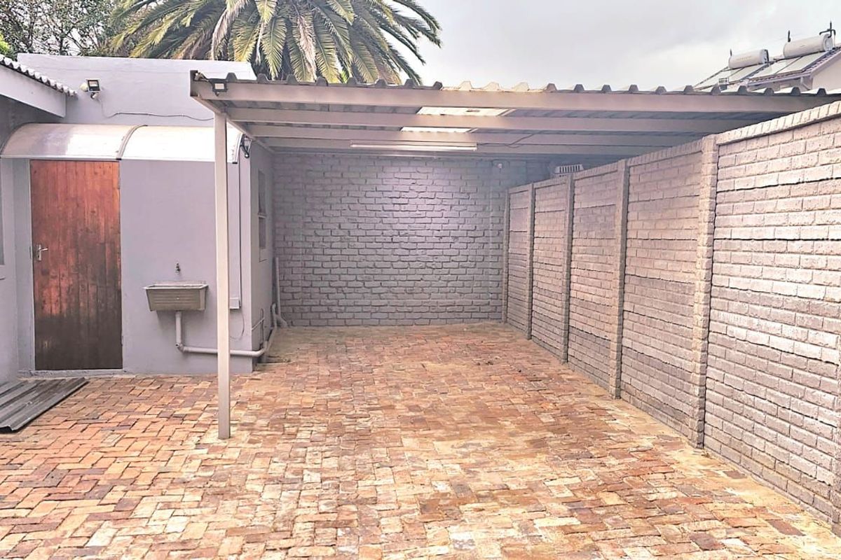 A paved outdoor area featuring a covered carport structure, brick boundary walls, and a utility sink attached to the exterior wall.