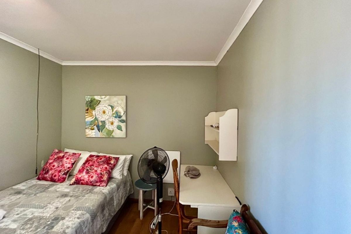 A functional bedroom featuring light green walls, wooden flooring, and a built-in wall-mounted shelving unit.