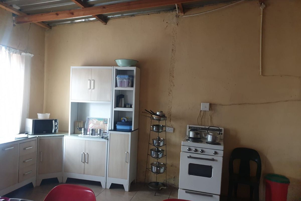 A basic kitchen area featuring a freestanding stove and simple cabinetry with exposed roof beams and visible wall cracks.