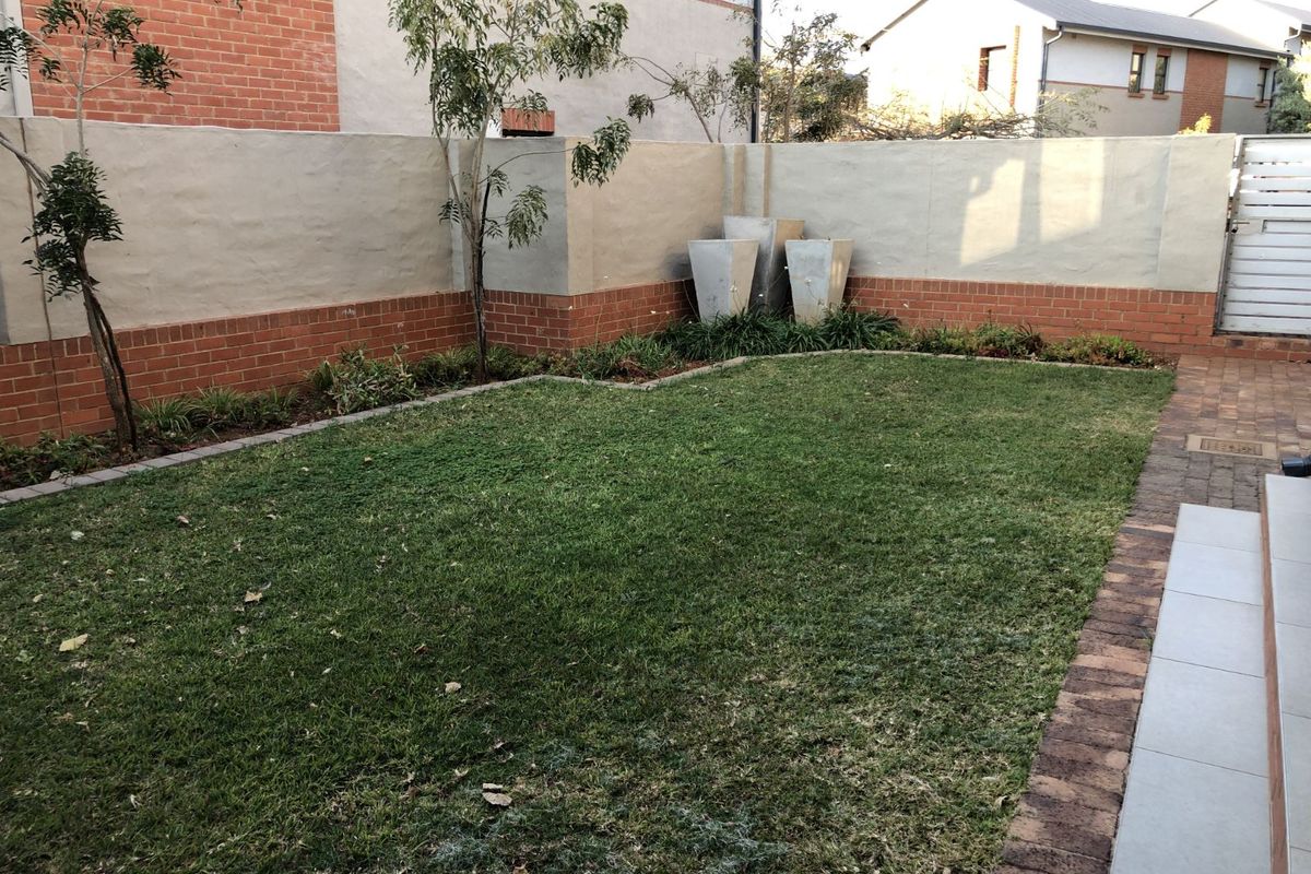 A private rear garden featuring a manicured lawn, brick-edged borders, and high perimeter walls, providing a secure and low-maintenance outdoor space.