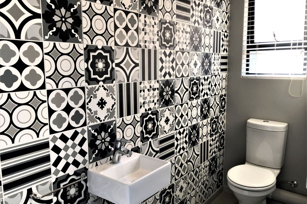A modern guest bathroom featuring striking monochrome patterned wall tiles, a wall-mounted basin, and a standard toilet.