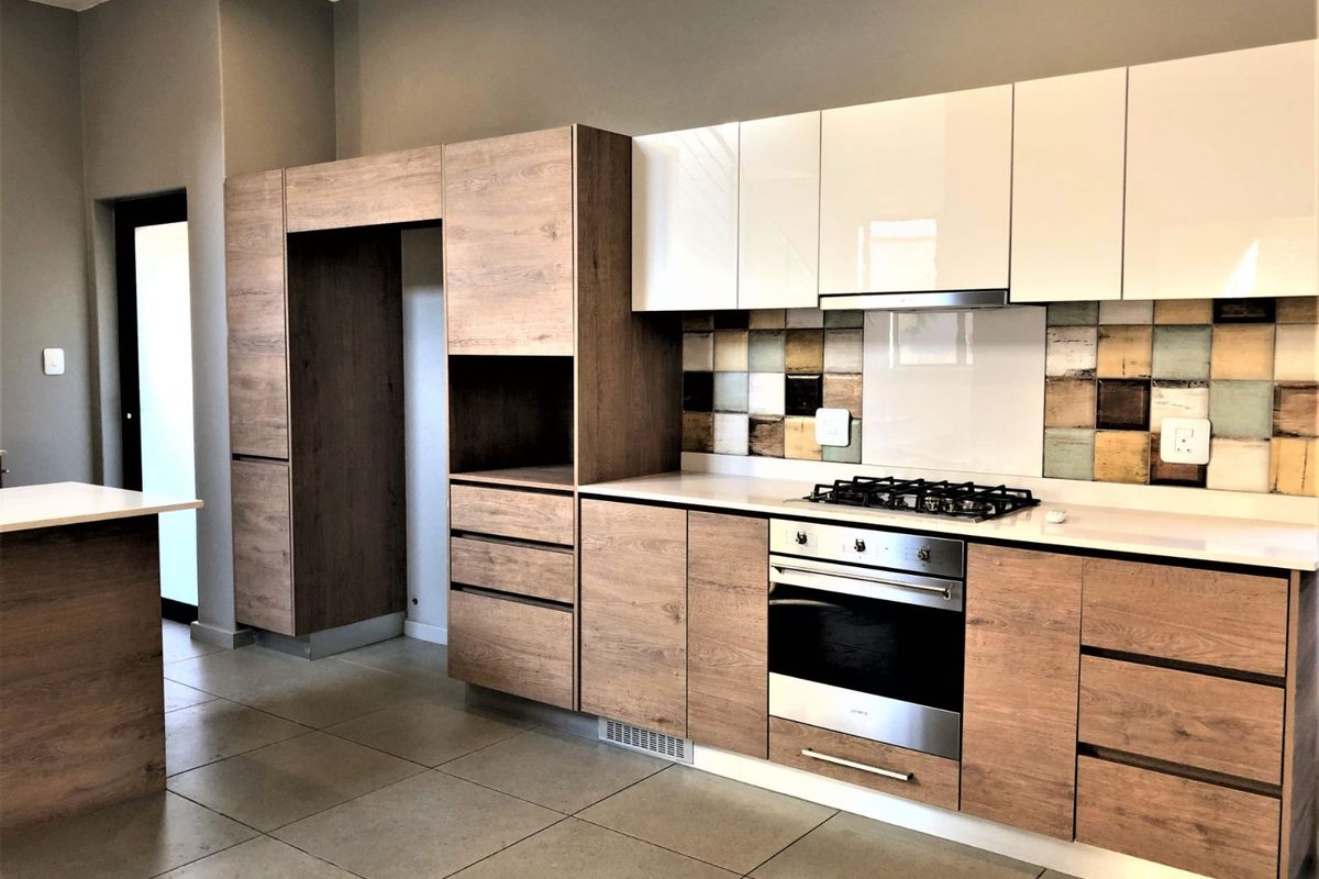 Modern kitchen featuring wood-grain cabinetry, white high-gloss upper cabinets, integrated oven, gas hob, and a decorative mosaic tile backsplash.