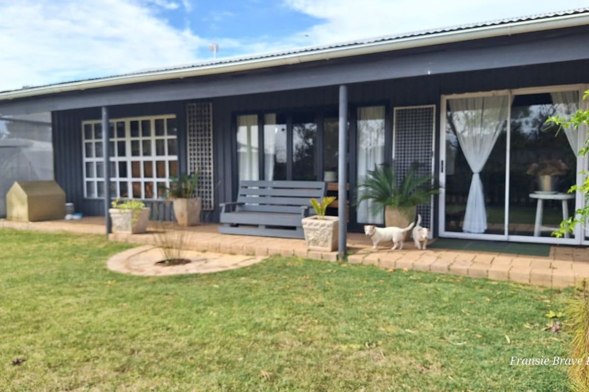 A rear view of the farmhouse featuring a covered patio area with paved flooring, sliding glass doors, and dark exterior cladding.