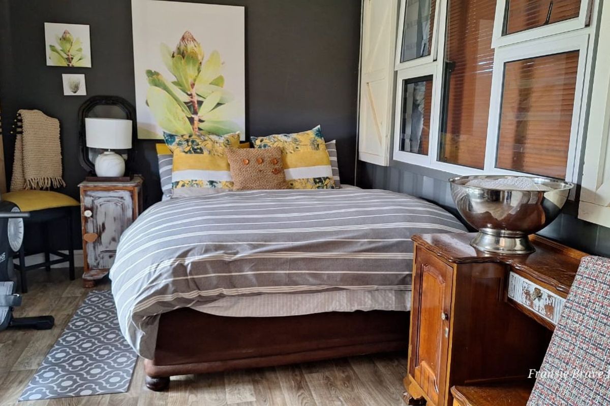 A cozy bedroom featuring dark accent walls, wood-look flooring, and white shutter-style window treatments.