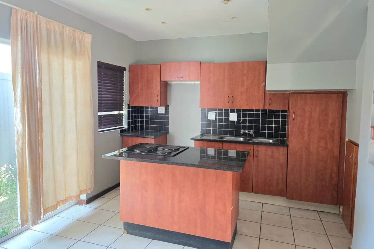 Kitchen featuring wooden cabinetry, black tiled backsplash, granite countertops, a central island with a built-in hob, and tiled flooring with direct patio access.