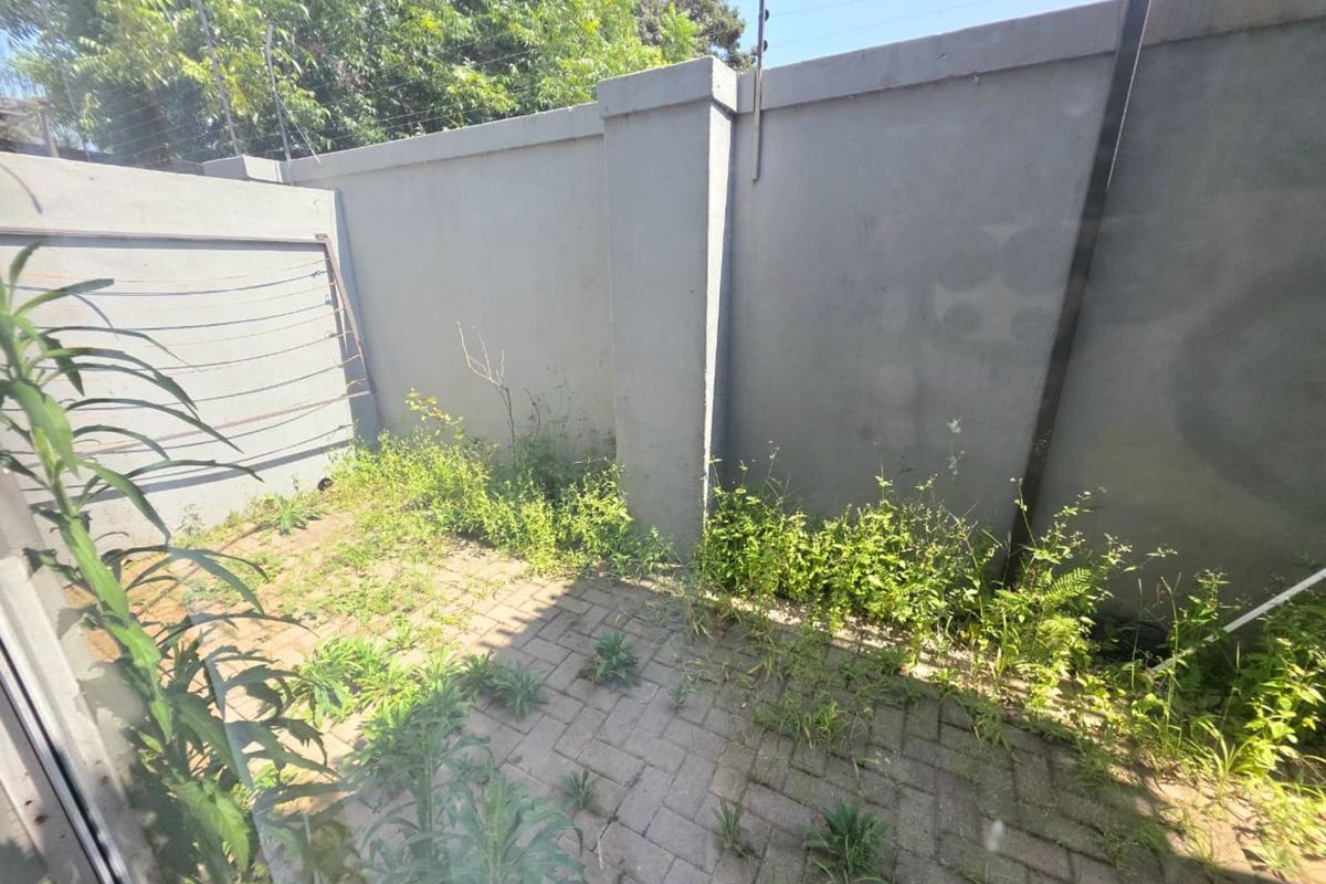 A private rear courtyard area featuring paved flooring, a high boundary wall with security fencing, and a wall-mounted drying rack.