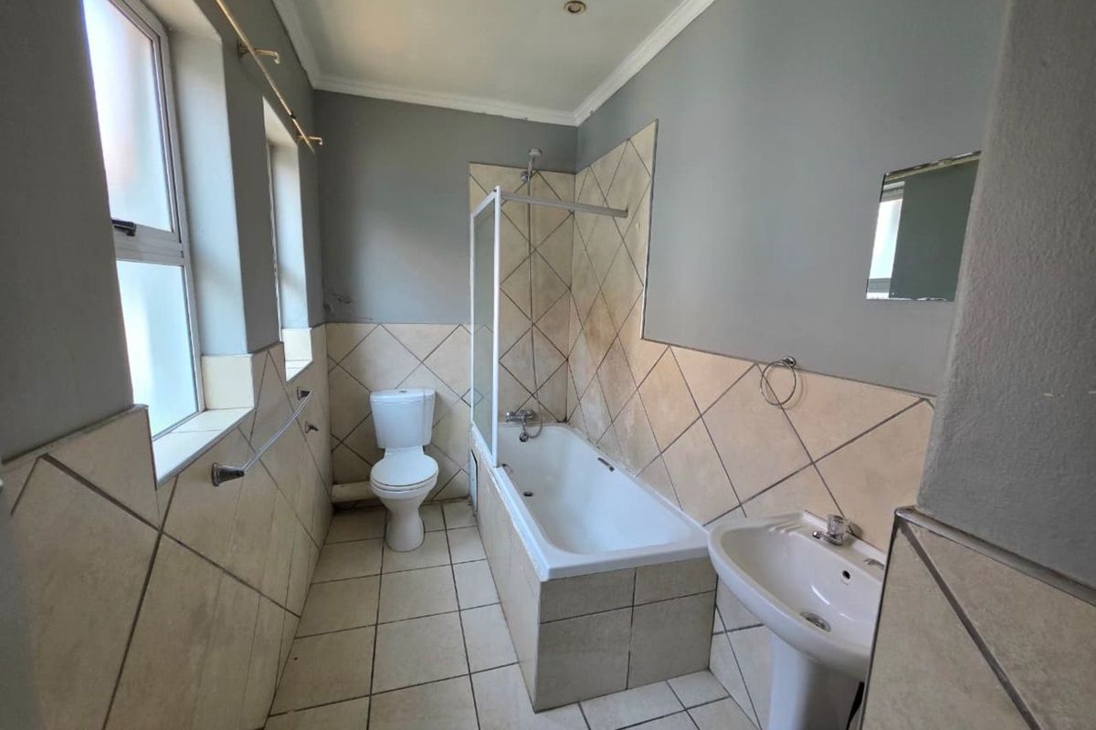 A functional bathroom featuring a bathtub with shower screen, pedestal basin, and toilet, finished with neutral wall and floor tiling.