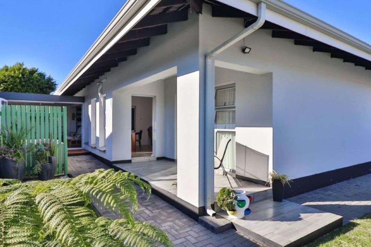 A well-maintained rear exterior view featuring a covered patio area with tiled flooring, paved walkways, and a green privacy fence.