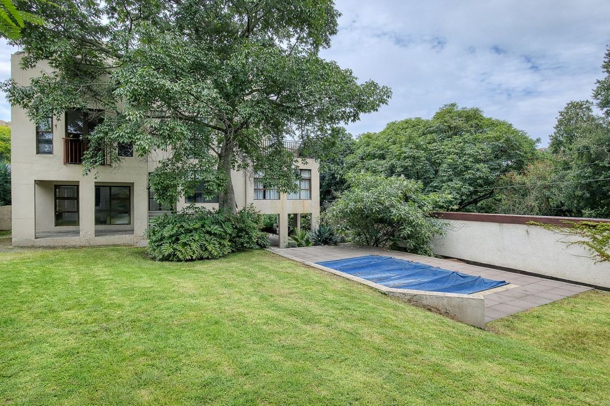 Rear garden view featuring a lawn, mature trees, and a swimming pool with a protective cover, set against the multi-story residential building.