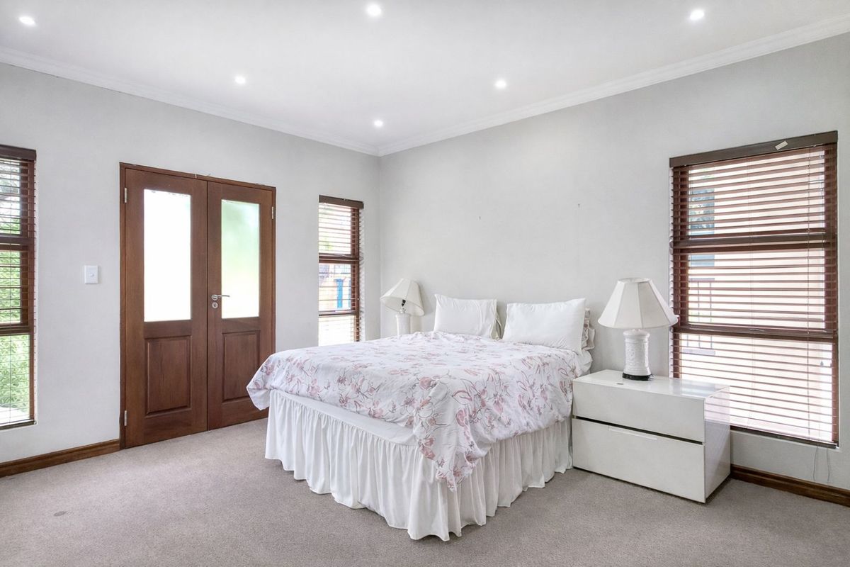 A bright and spacious bedroom featuring neutral carpeting, recessed ceiling lighting, and double doors leading to an outdoor area.