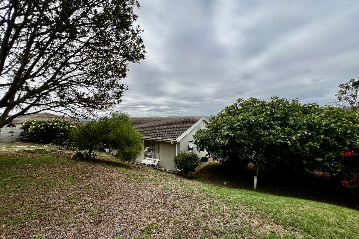 A view of the rear exterior of the house, featuring a tiled roof, established garden, and mature trees on a sloped plot.