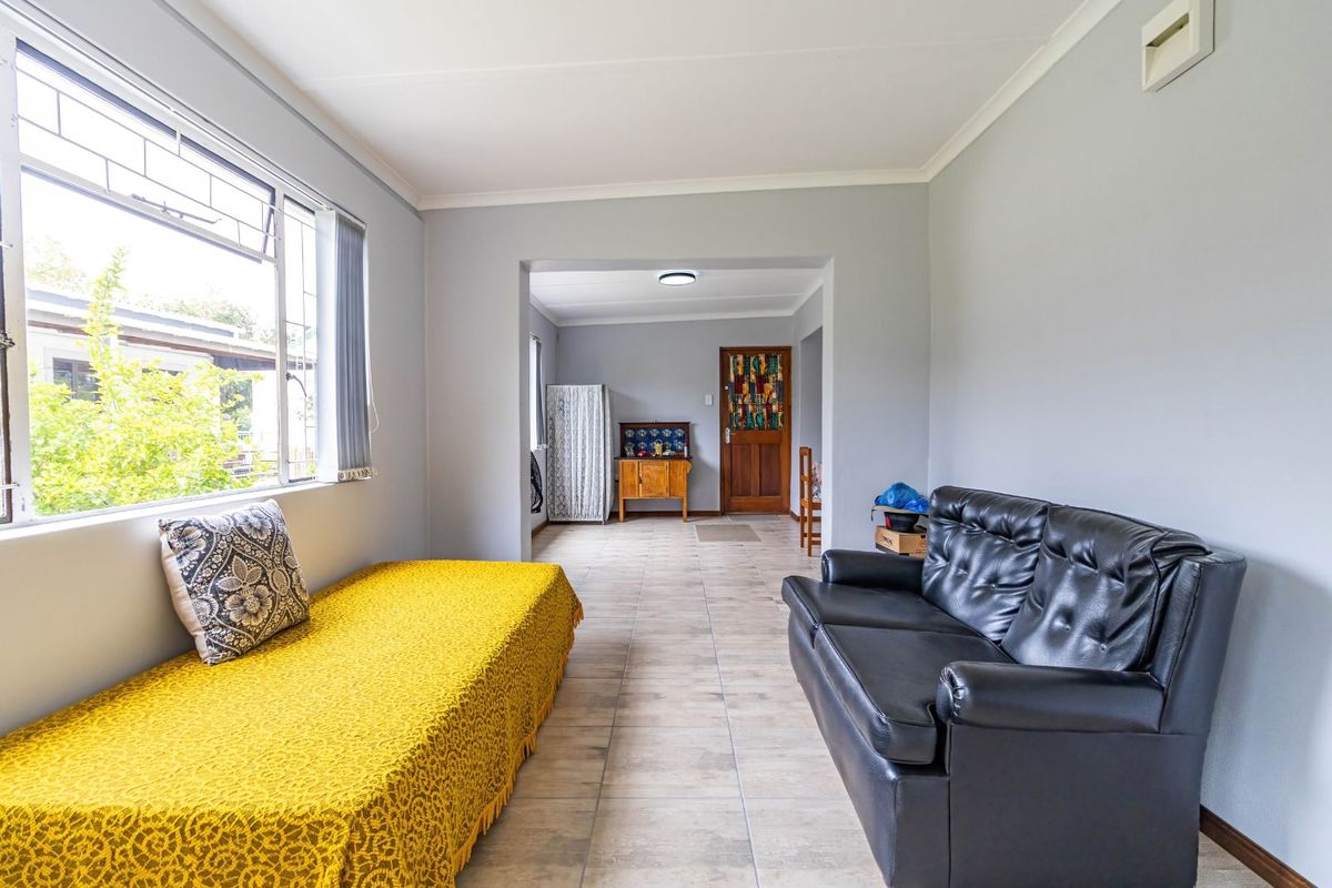 A bright living area featuring tiled flooring, large windows, and a seamless transition into an adjacent room, offering a functional and open layout.