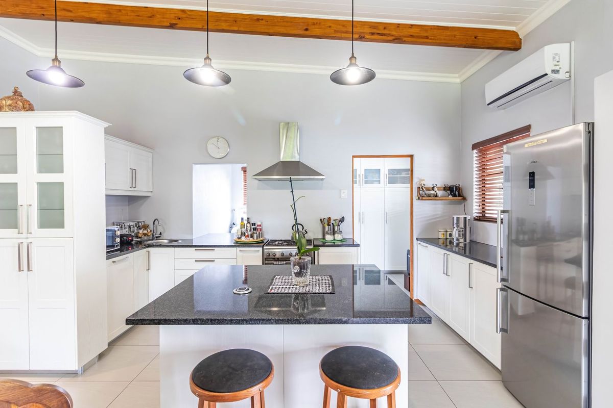 Modern kitchen featuring white cabinetry, granite countertops, a central island, stainless steel extractor fan, and exposed timber ceiling beams.