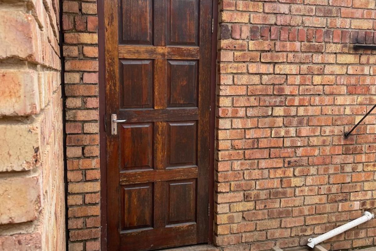 A side entrance featuring a solid timber door, brick facade, and a protective polycarbonate awning over the doorway.