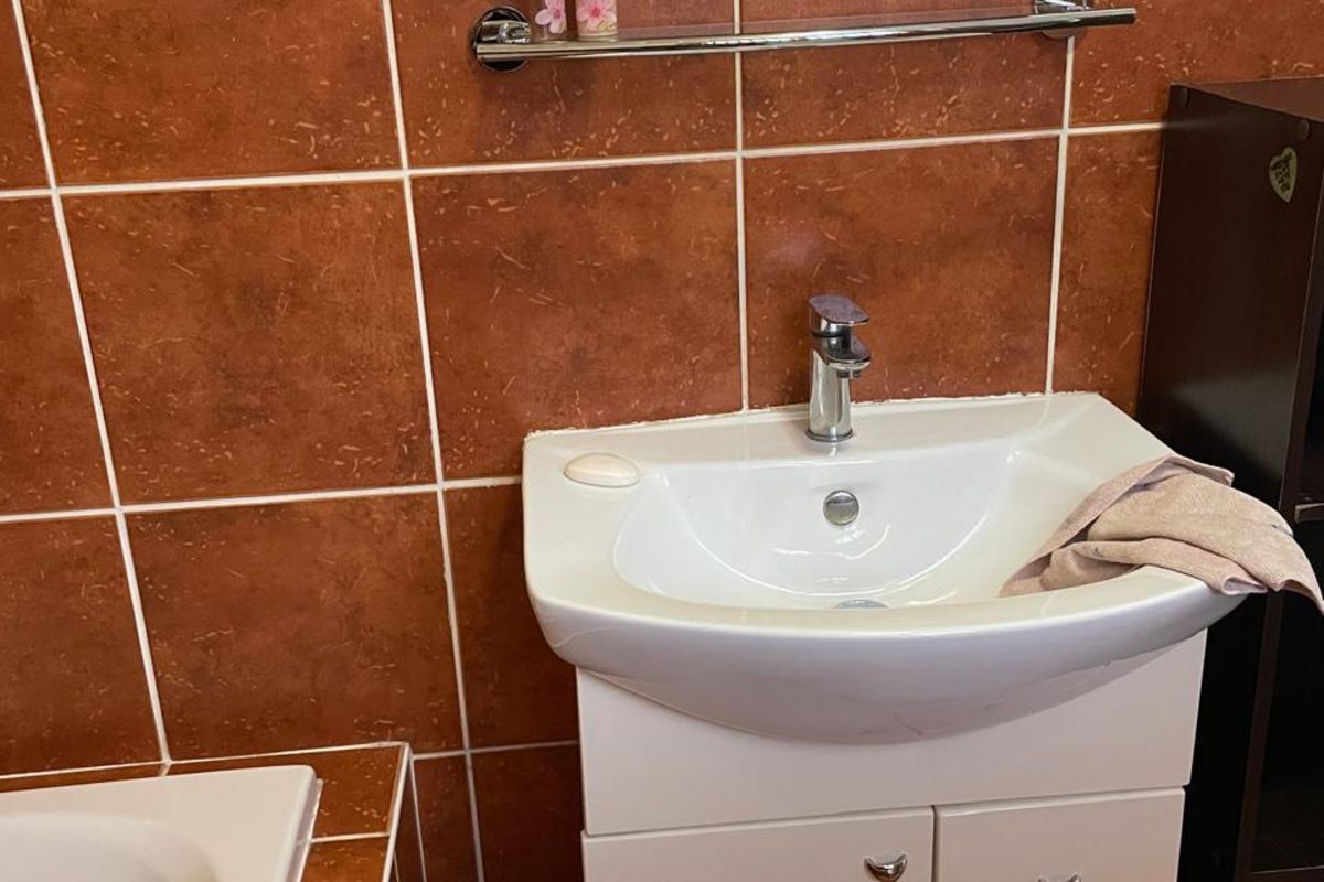 A bathroom vanity area featuring a white basin, chrome faucet, and dark terracotta-toned wall tiles.