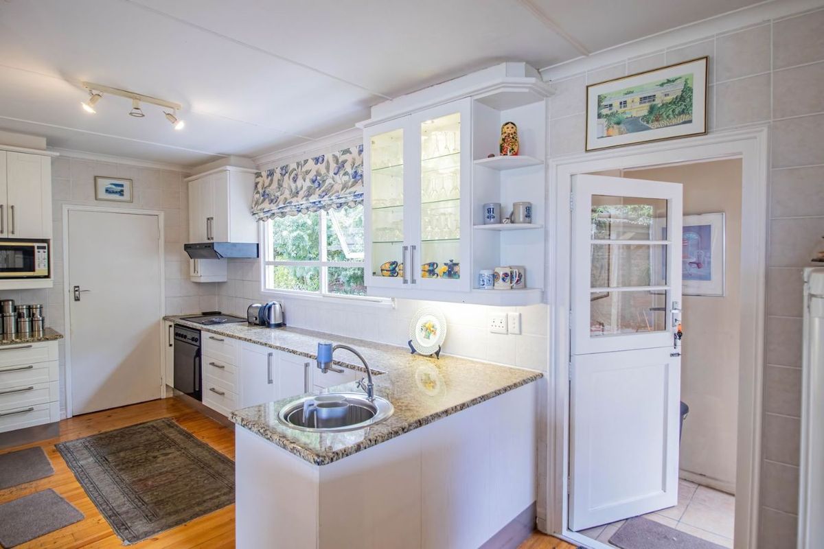 A well-maintained kitchen featuring white cabinetry, granite countertops, a built-in oven, extractor fan, and a stainless steel sink with a breakfast bar.