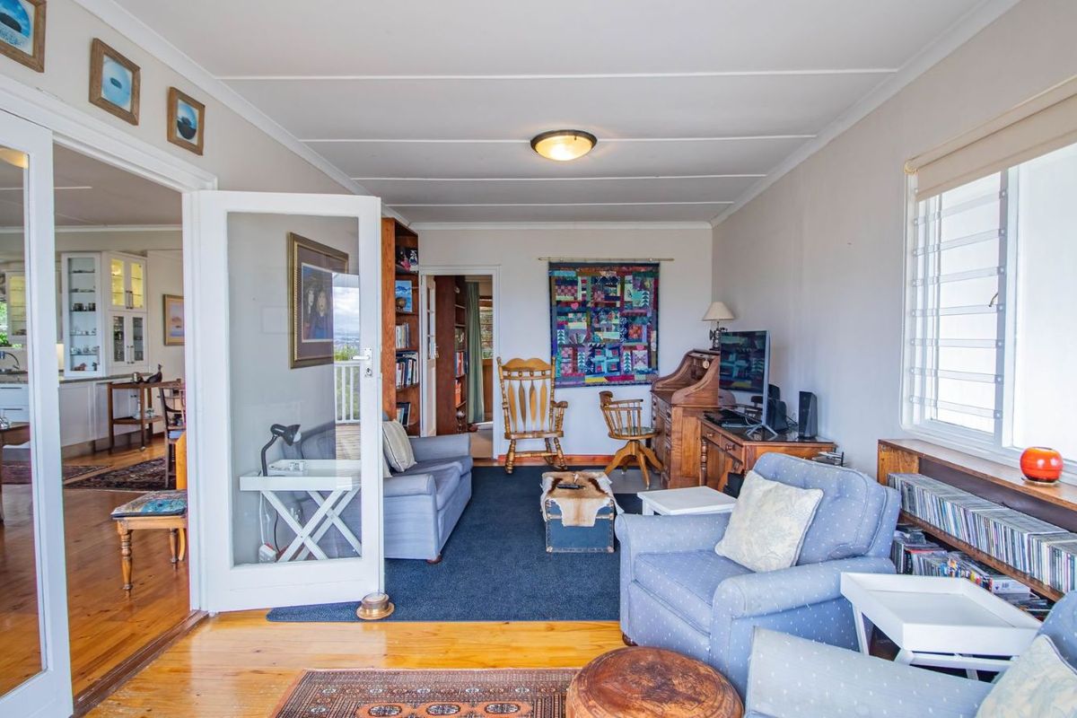 A comfortable living room featuring polished timber flooring, large windows, and direct access to the adjacent kitchen area through glass-paneled doors.