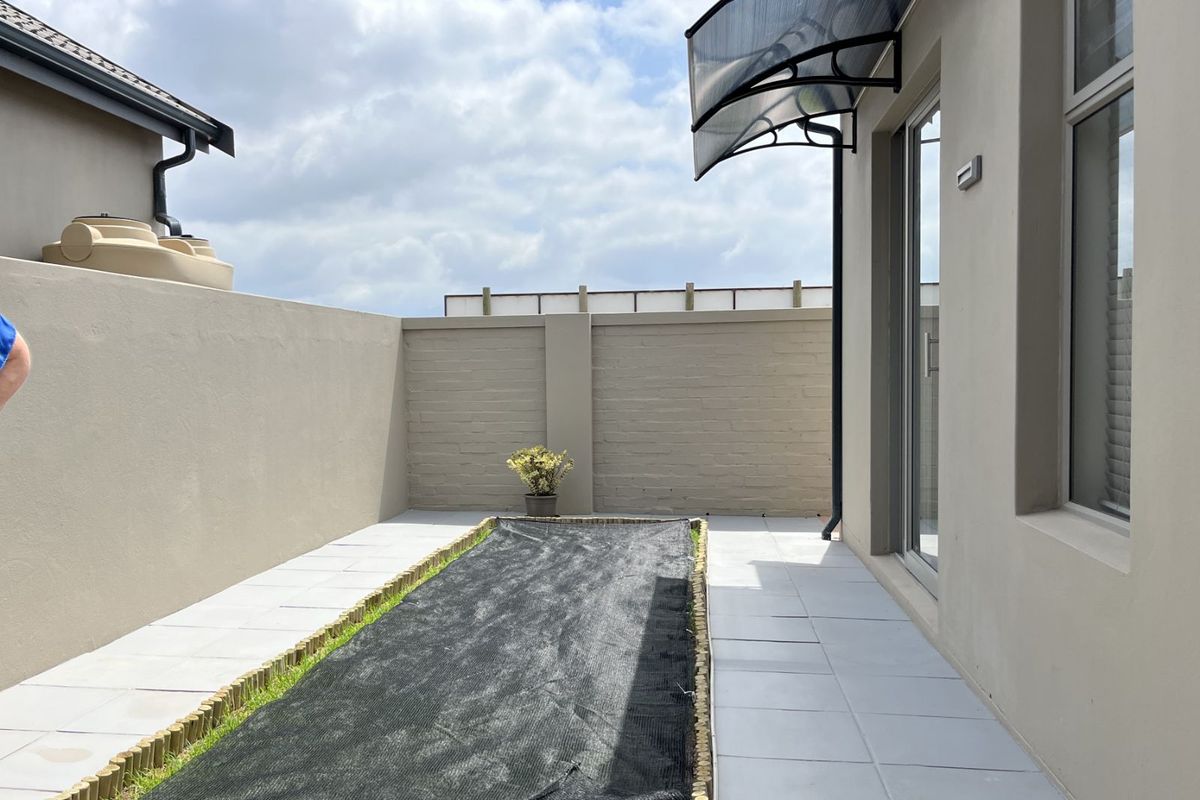 A private rear courtyard featuring paved flooring, a small garden bed with a protective cover, and a modern door awning.