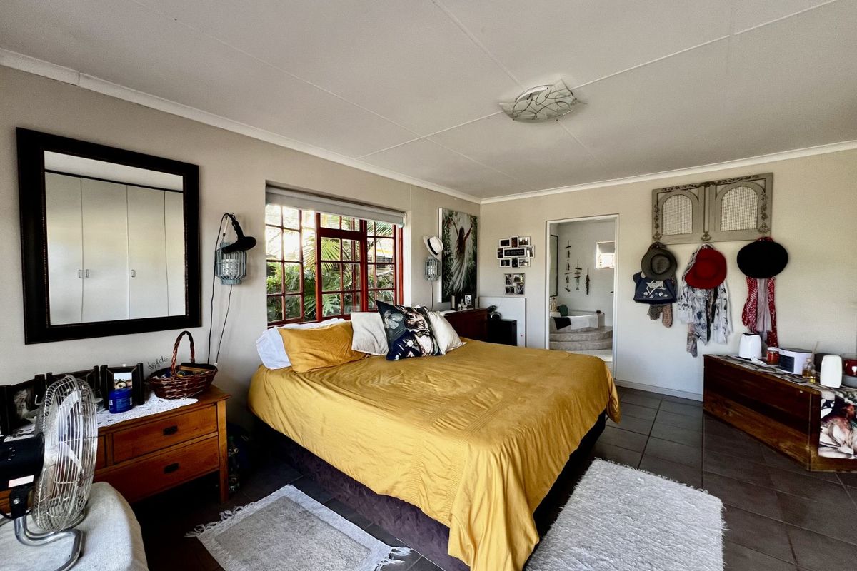 Spacious bedroom featuring tiled flooring, large window with red frames, and direct access to an en-suite bathroom.