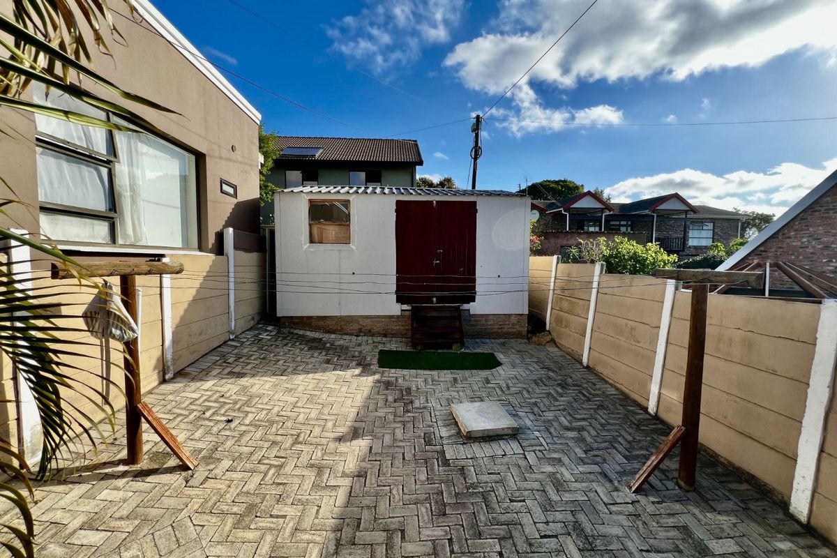 A paved rear courtyard area featuring a detached utility structure and fixed washing line posts.
