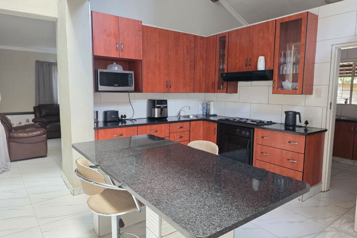 A functional kitchen featuring dark granite countertops, wooden cabinetry, a built-in oven with extractor fan, and a breakfast bar island.