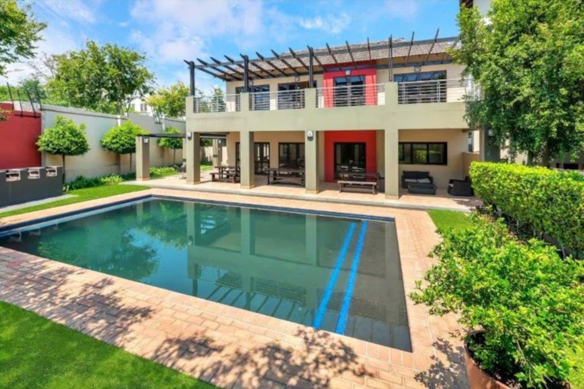 Rear view of a two-story house featuring a swimming pool, covered patio area, and a balcony with a pergola structure.