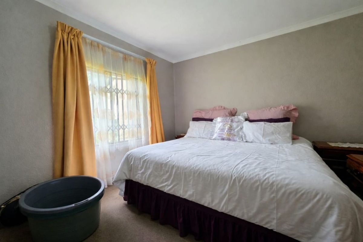 A standard bedroom featuring neutral wall tones, carpeted flooring, and a window fitted with security bars.