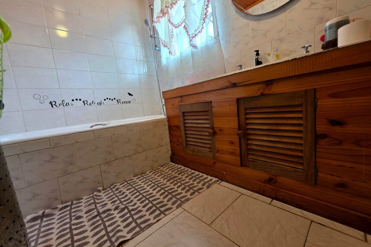 A functional bathroom featuring a built-in bathtub with shower attachment, tiled walls, and a wooden vanity cabinet with louvered doors.
