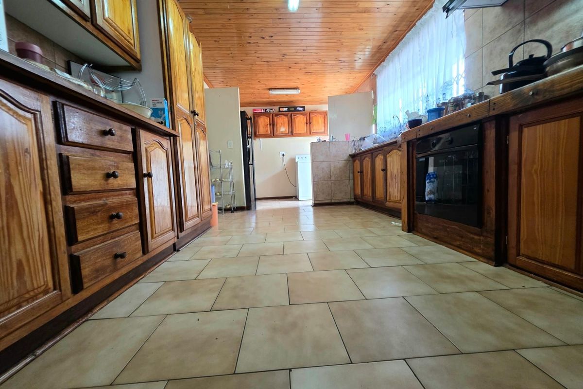 A functional kitchen featuring timber cabinetry, tiled flooring, and a timber-clad ceiling, offering a traditional aesthetic with ample storage space.