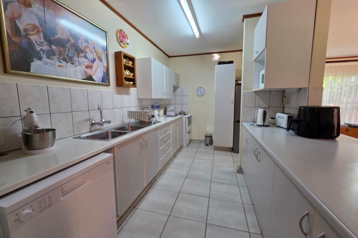 A functional galley-style kitchen featuring white cabinetry, tiled flooring, tiled splashbacks, and a double stainless steel sink.