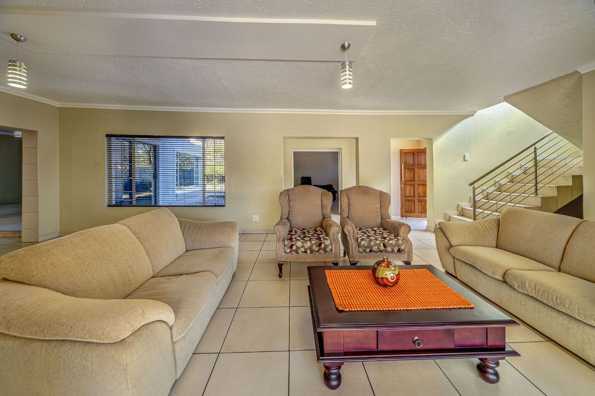 Spacious living room featuring tiled flooring, a staircase with metal balustrades, and neutral wall tones, providing a functional and open layout.