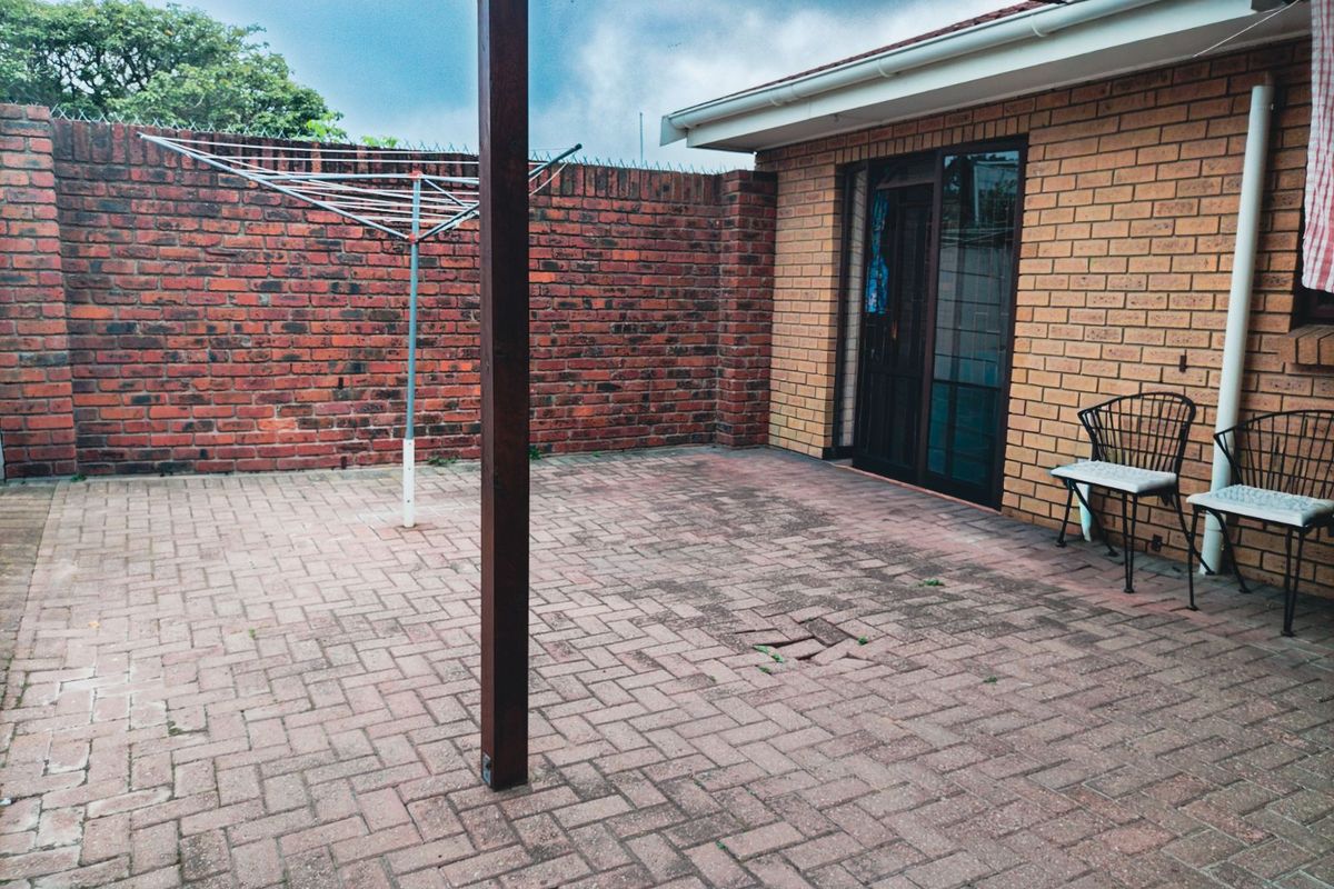 A paved rear courtyard area featuring a brick boundary wall, a rotary clothesline, and direct access to the home via a sliding glass door.